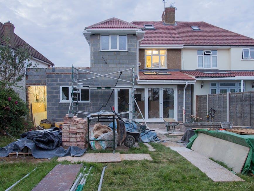 A construction excavator with a long arm and bucket attachment is positioned among a pile of rubble and debris in a garden area, surrounded by overgrown vegetation and leafless trees. The ground appea